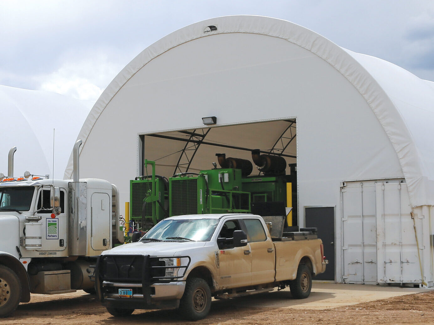 Trucks parked outside two ClearSpan truss arch buildings