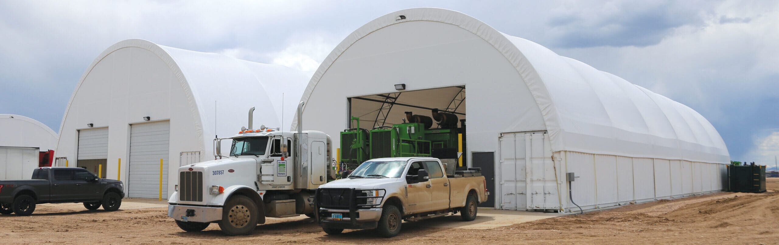 Trucks parked outside two ClearSpan truss arch buildings