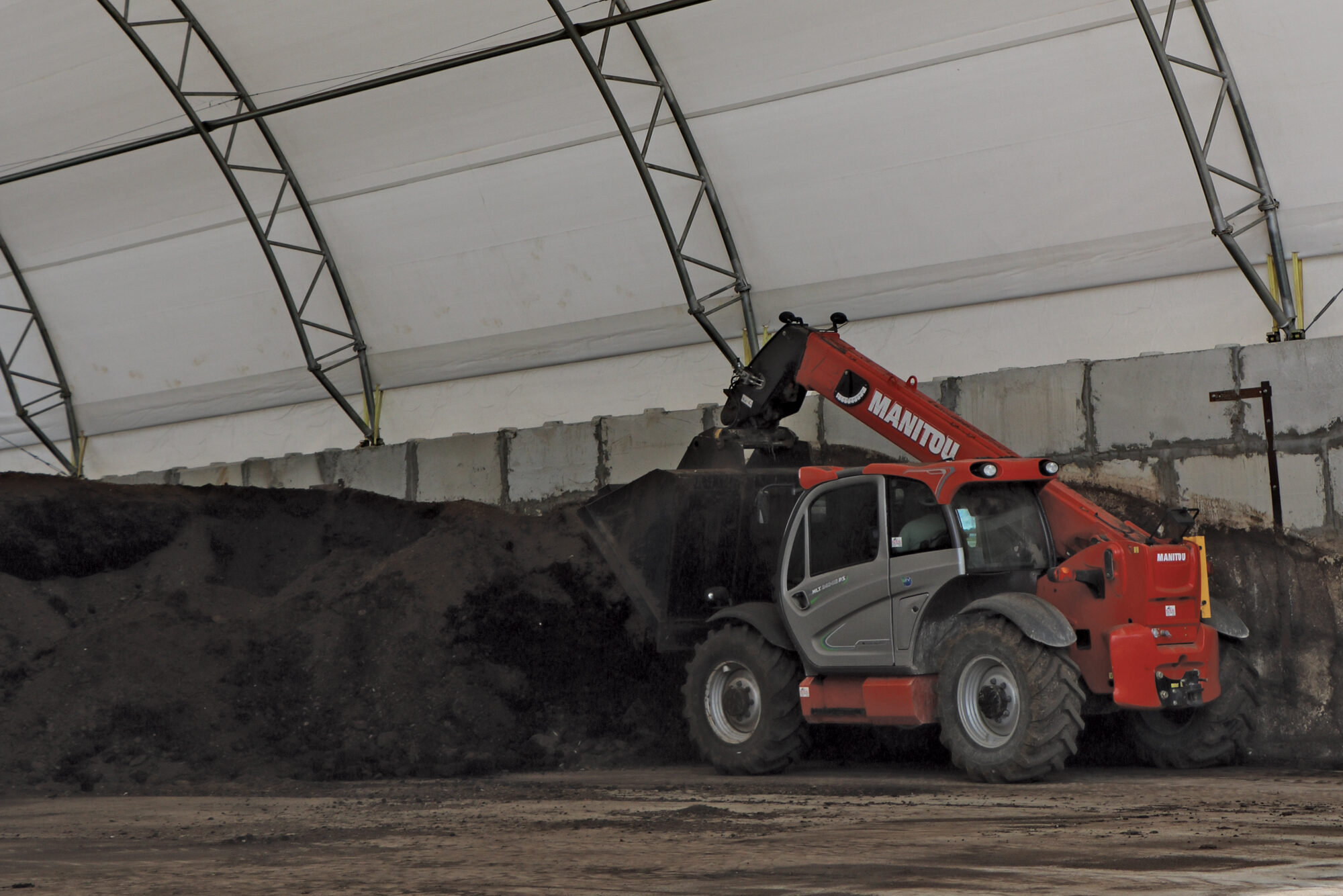 vehicle scooping compost material inside fabric structure