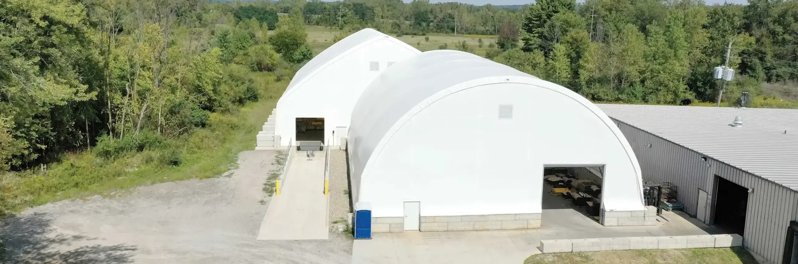 two white fabric warehouse buildings with trees and landscaping in the background