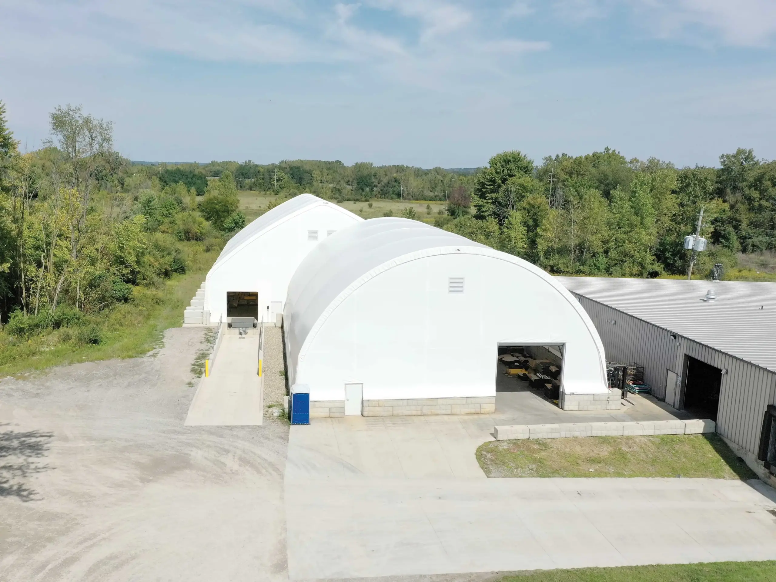 two white fabric warehouse buildings with trees and landscaping in the background