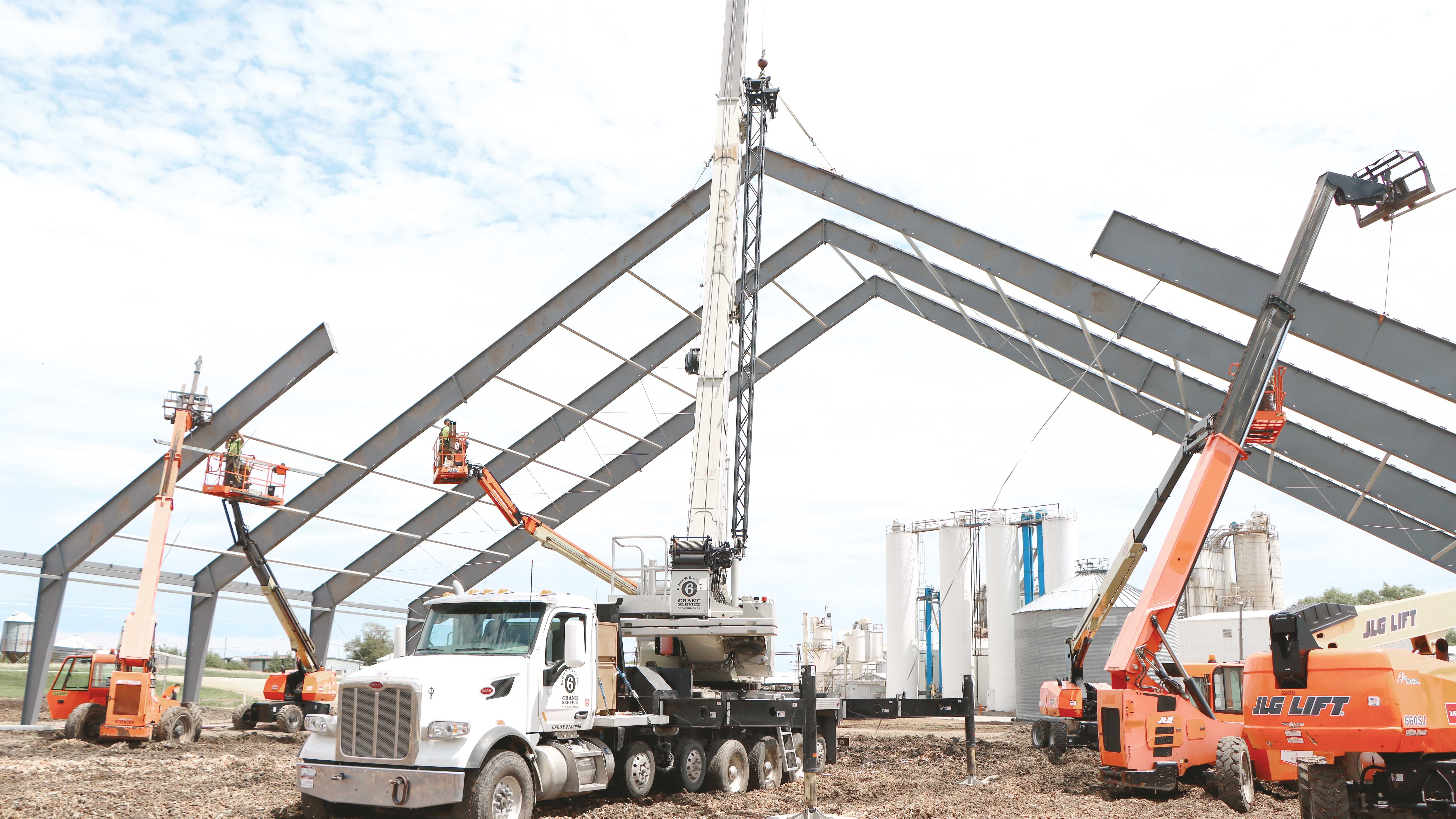 Ongoing installation of a ClearSpan HD Beam Building on a dirt lot; a truck with a crane and multiple lifts are parked underneath